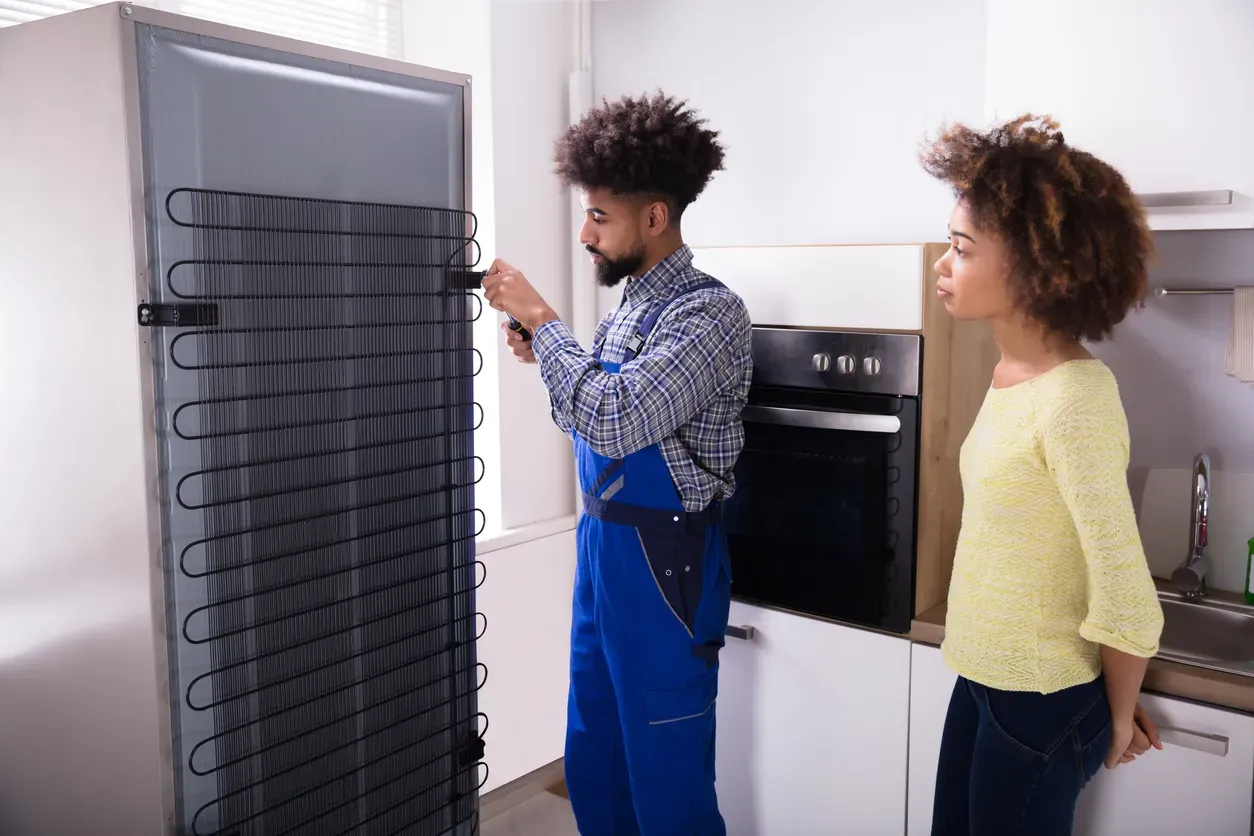 A close-up of refrigerator condenser coils being cleaned with a brush.